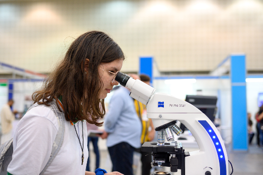 Imagem: menina com fardamento escolar observa microscópio