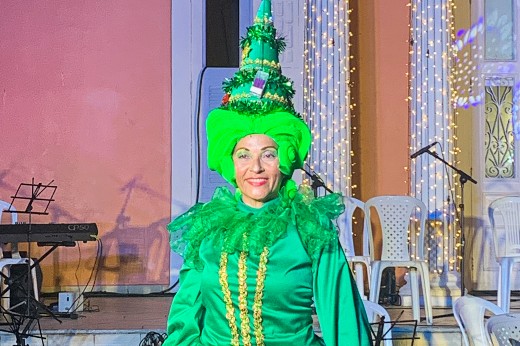 Atriz do grupo VemArt & Alegra+ aparece em frente ao prédio da Reitoria, vestindo figurino totalmente verde, composto por vestido de mangas compridas, peruca e chapéu em forma de cone
