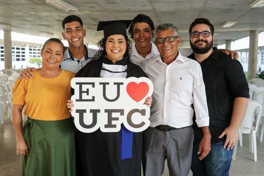 Imagem: Formanda Natacha Falcão posa junto à família e ao namorado, segurando uma placa onde se lê Eu Amo UFC (com a figura de um coração vermelho no lugar da palavra "amo")