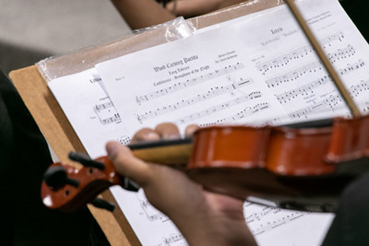 Imagem: livro de partitura de música e imagem de uma mão e um violino sendo tocado 