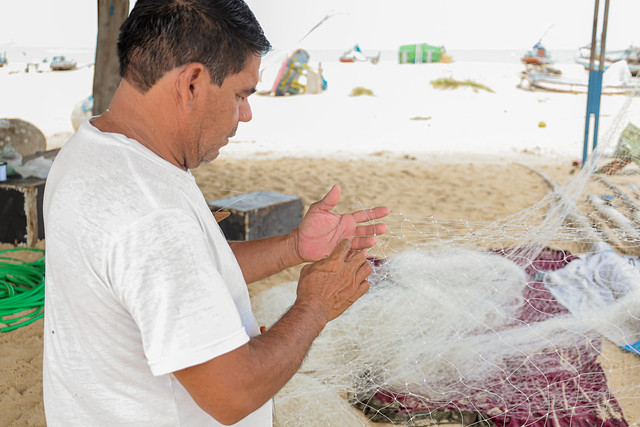 Imagem: pescador costura rede de pesca