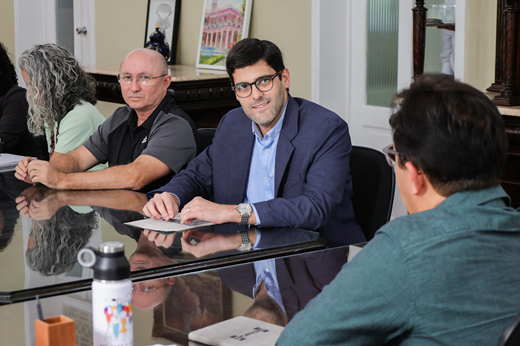 Imagem: Sentado à mesa, o superintendente João Gabriel Rocha conversa com o reitor Custódio Almeida (de costas)