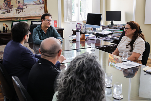 Imagem: Participantes da reunião sentados à mesa de costas; de frente estão apenas o reitor Custódio Almeida e a secretária Aliny Abreu