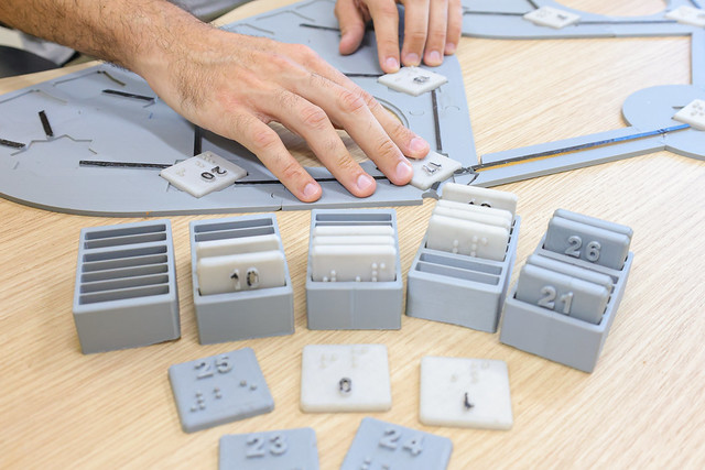 Imagem: mão manuseia peças táteis que auxiliam estudantes com deficiência visual no ensino da computação