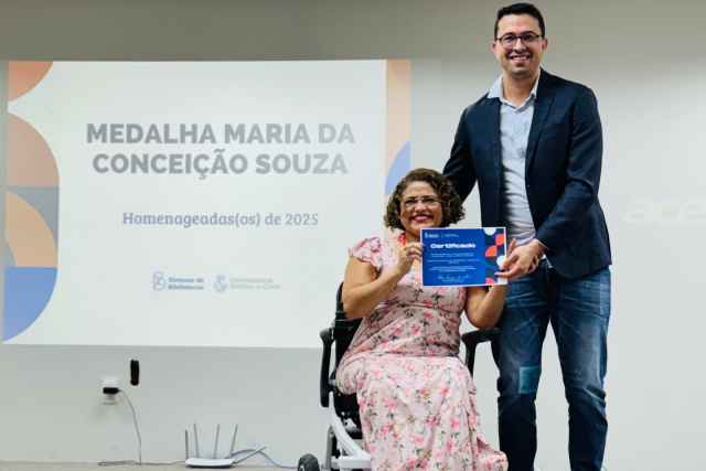 Imagem: mulher cadeirante recebe medalha e certificado de homem em pé ao lado dela