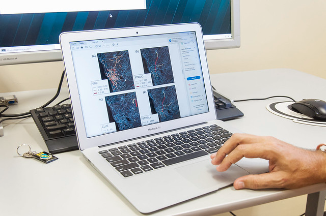 O resultado considera o impacto das pesquisas a partir do número de citações (Foto: Viktor Braga/UFC) Imagem: Fotografia mostra uma mão masculina sobre o teclado de um notebook prateado. Na tela do computador portátil, aparecem gráficos científicos em forma de imagens coloridas com linhas e pontos interligados, acompanhados de legendas e siglas. O notebook está sobre uma mesa clara, ao lado de um teclado preto, um mouse e um chaveiro com crachá. Ao fundo, vê-se parte de um monitor maior.