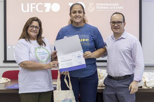 Imagem: Professora Marilene Soares (pró-reitora de Gestão de Pessoas) e professor Sandro Wagner (diretor do Campus de Crateús) entregam certificado de tempo de serviço a servidora da unidade, durante evento da Progep.