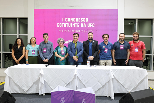Imagem: De pé, no palco, da esquerda para a direita: Yasmin Santos (estudante de Direito e representante discente no Conselho Universitário e na Comissão Organizadora); Heveline Ribeiro (servidora do Instituto de Cultura e Arte [ICA] e representante dos técnico-administrativos no Conselho Universitário e na Comissão Organizadora); professor Gabriel Paillard (diretor do Instituto UFC Virtual e representante docente na Comissão Organizadora); professora Diana Azevedo (vice-reitora); professor Custódio Almeida (reitor); Daniel Fonsêca (coordenador de Articulação Política do Gabinete da Reitoria e presidente da Comissão Organizadora); professor André Ferreira (presidente da ADUFC-Sindicato e representante sindical na&nbsp;Comissão Organizadora); Carlos Alberto Florêncio (coordenador-geral do Sintufce e representante sindical na&nbsp;Comissão Organizadora) e Nathan de Deus (secretário-geral do Diretório Central dos Estudantes e representante da entidade&nbsp;na&nbsp;Comissão Organizadora).&nbsp;
