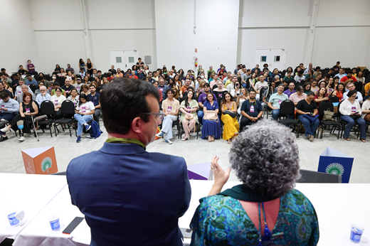 Imagem: Foto mostra o reitor e a vice-reitora de costas no palco; à frente, olhando para eles, estão os delegados e ouvintes do I Congresso Estatuinte sentados.