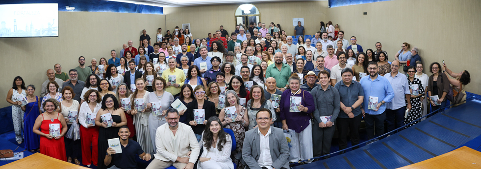 Imagem: Sentados ao centro, estão os professores Cavalcante Júnior, Juliana Diniz e Custódio Almeida; ao redor, de pé, os autores da coletânea seguram seus exemplares. 