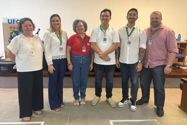 O sorteio definiu os pontos que serviram de base para o desenvolvimento da prova dissertativa, sendo realizado de forma pública e devidamente registrado (Foto: Divulgação) Imagem: Seis pessoas posam lado a lado para foto em uma sala institucional da UFC. Todas usam crachá e vestem roupas casuais ou sociais. Ao fundo, há uma mesa, cadeiras e um banner com a identidade visual da universidade.