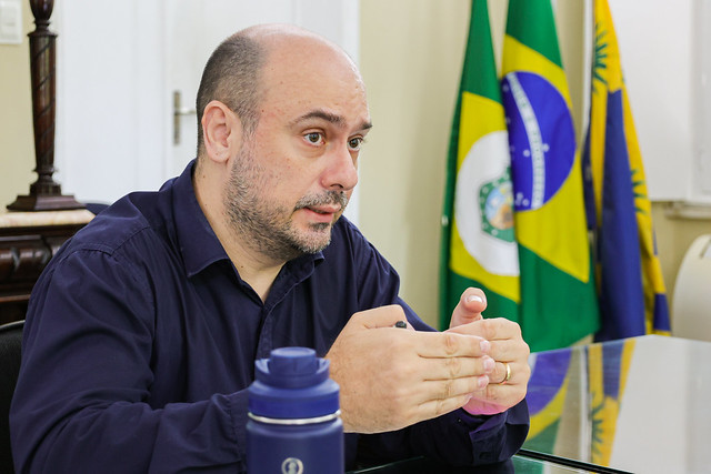 Coordenador do projeto pela UFC, o professor Bruno Bertoncini considera o projeto um dos mais ambiciosos do país na área de qualidade do ar e saúde pública (Foto: Gutiérrez Reges/UFC) Imagem: Homem branco, de meia-idade, com cabeça parcialmente calva e barba curta, veste camisa social azul-escura e está sentado à mesa, em ambiente institucional. Ele gesticula com as mãos enquanto fala, demonstrando expressão atenta e concentrada.