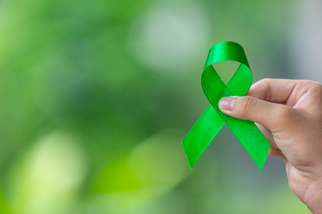 Imagem: mão segurando fita verde, símbolo da campanha Julho Verde