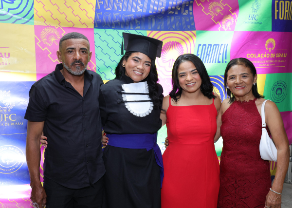 Além de rito simbólico, as colações são um momento importante para amigos e familiares dos concludentes, ao instituir um espaço coletivo de celebração (Foto: Victor Braga/UFC) Imagem: quatro pessoas em uma cerimônia de colação de grau da UFC. Ao centro, uma mulher usa beca e capelo, acompanhada por um homem, uma mulher de vestido vermelho e outra de vestido vinho.