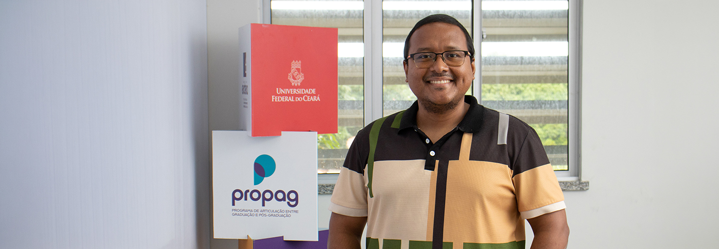 Aluno negro da pós-graduação posa tendo ao fundo quadrados com a marca da UFC e do Propag