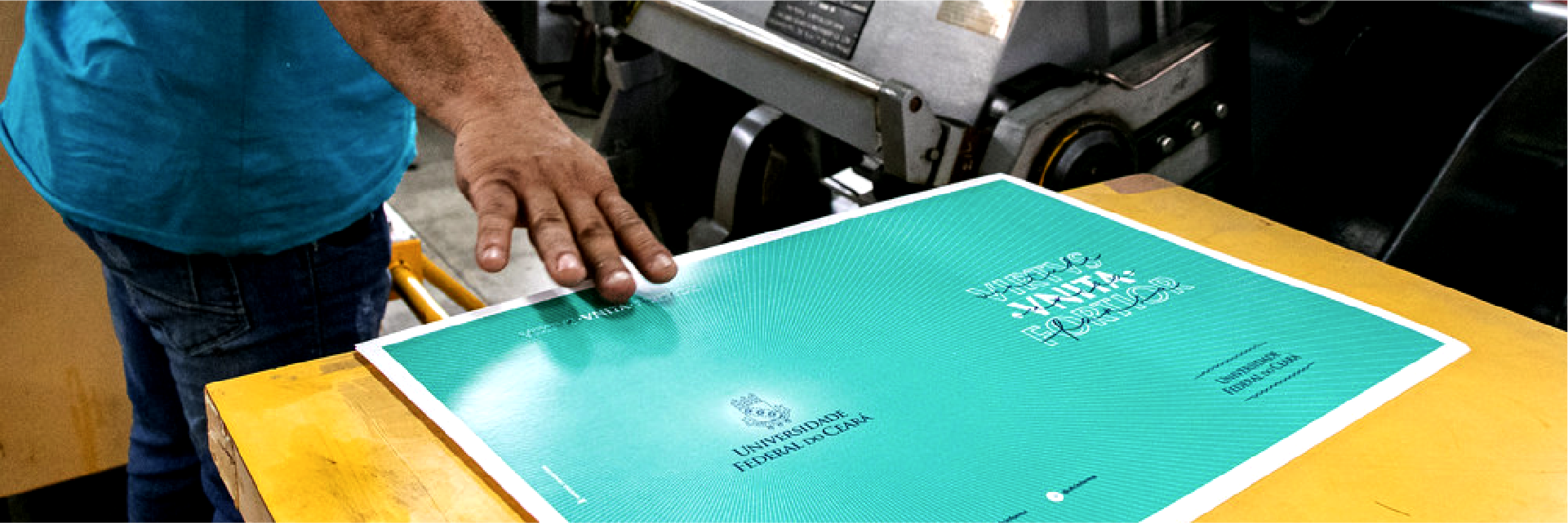 Detalhe de mão e papel em mesa com equipamento de produção gráfica