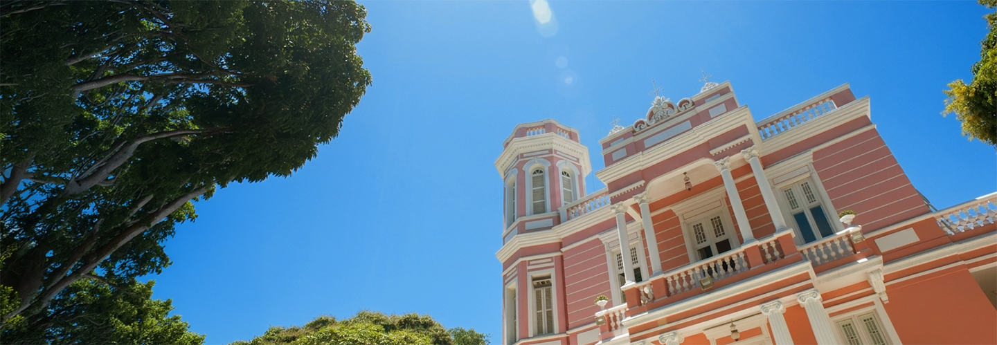 Fotografia visualizando o segundo andar da Reitoria tendo como fundo céu azul e árvora frondosa